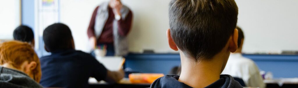 taylor-flowe-4nKOEAQaTgA-unsplash Leerlingen zitten in een klaslokaal met hun rug naar de camera.